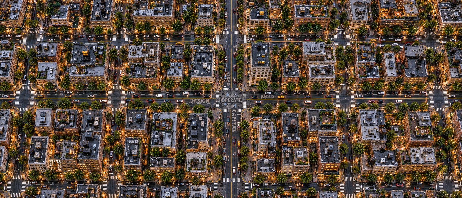 An aerial view of a city grid at dusk where the streets spell "Design · Build · Deals · Capital · Operate."